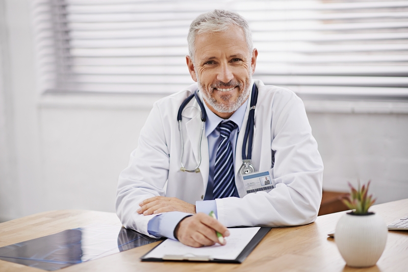 Healthcare, portrait and male doctor with a clipboard in his office analyzing xray document in hospital. Confidence, smile and professional mature man medical worker with paperwork by desk in clinic